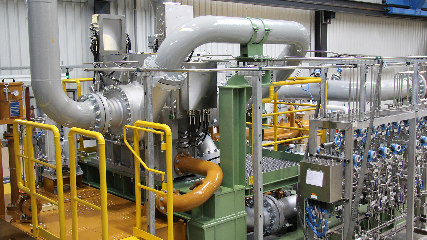 A integrally geared centrifugal compressor with process gas lines and DGS panel on the test field can be seen.