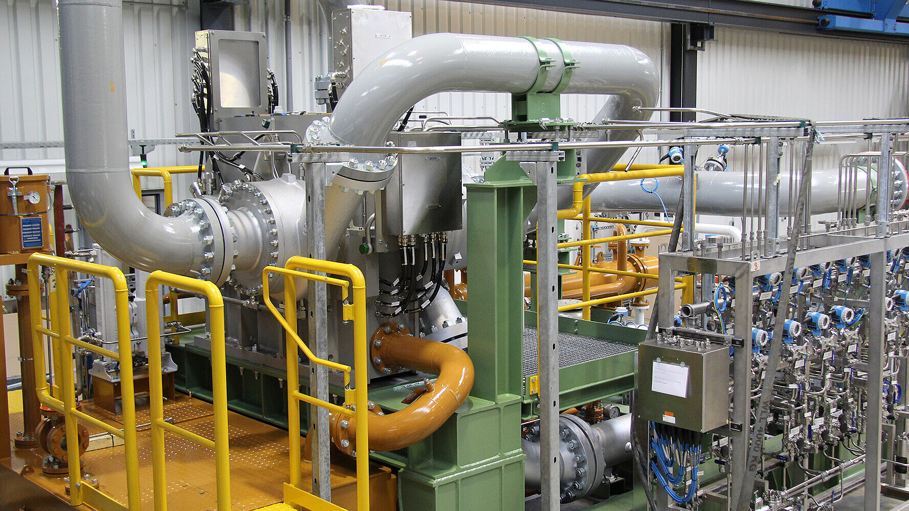 A integrally geared centrifugal compressor with process gas lines and DGS panel on the test field can be seen.