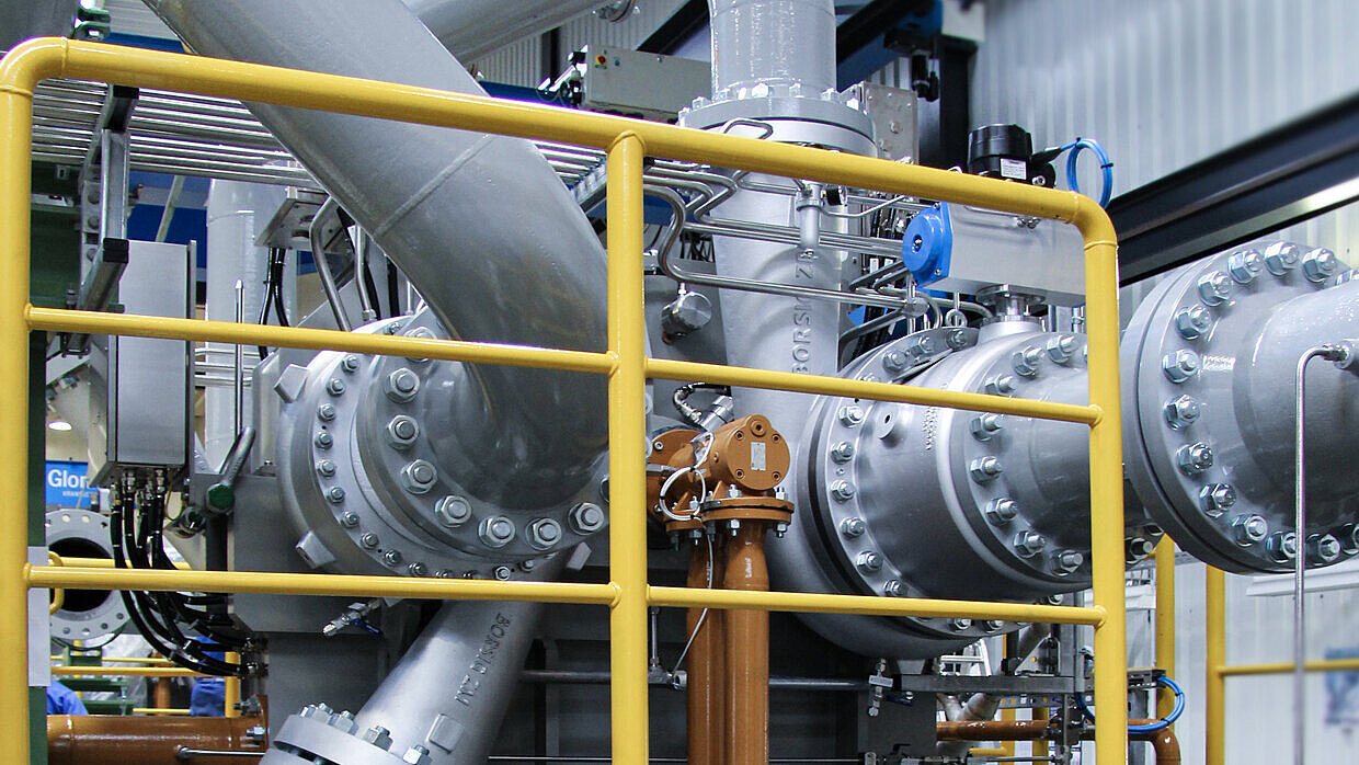 Shown are gray process gas lines of an integrally geared centrifugal compressor incl. yellow fall protection in the focus. The compressor is located on the test field.