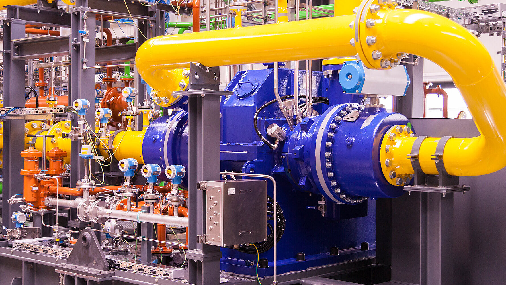 A blue 2-stage integrally geared centrifugal compressor with yellow process gas lines and measuring equipment is shown, installed on a skid.