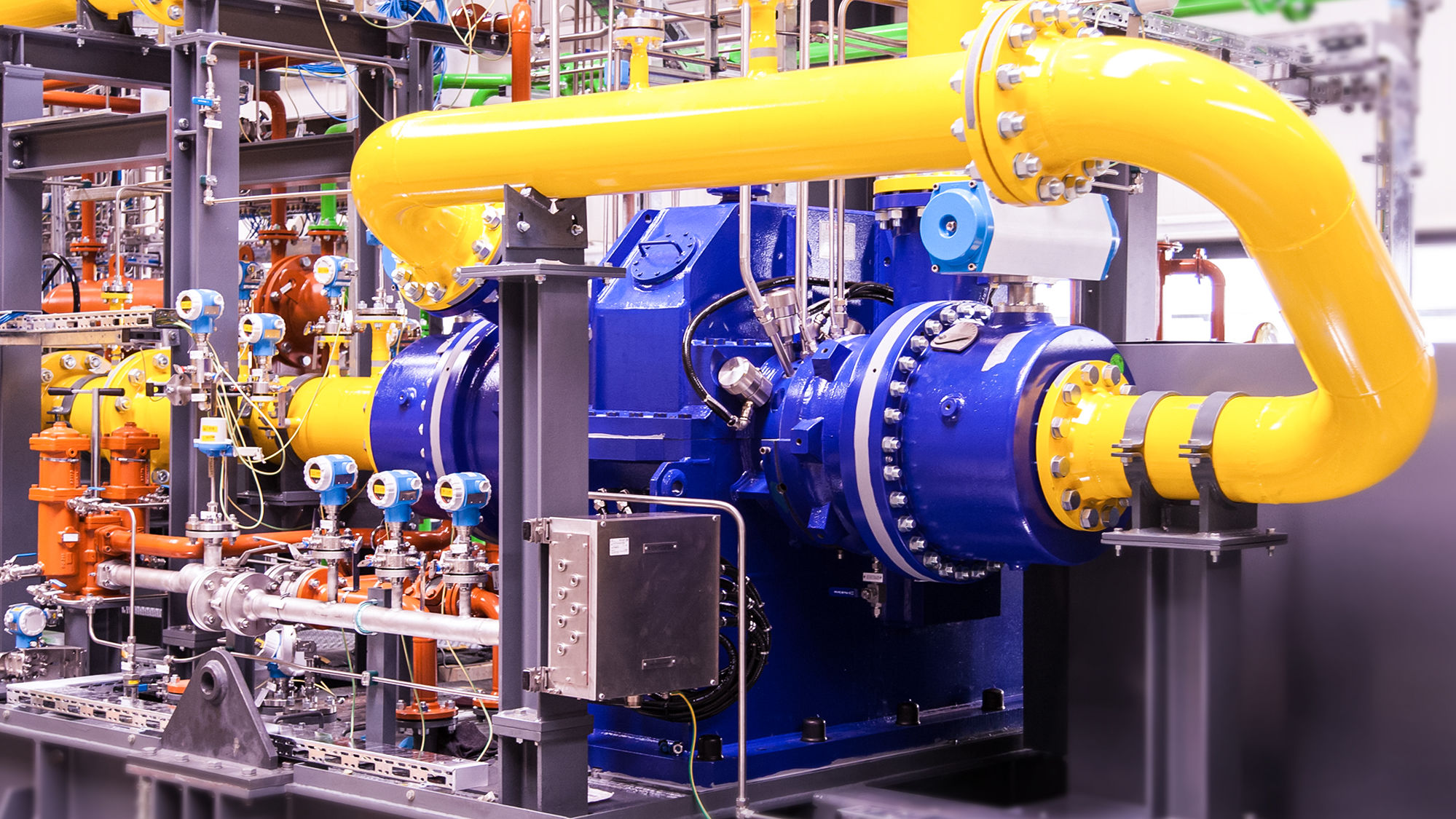 A blue 2-stage integrally geared centrifugal compressor with yellow process gas lines and measuring equipment is shown, mounted on a skid.