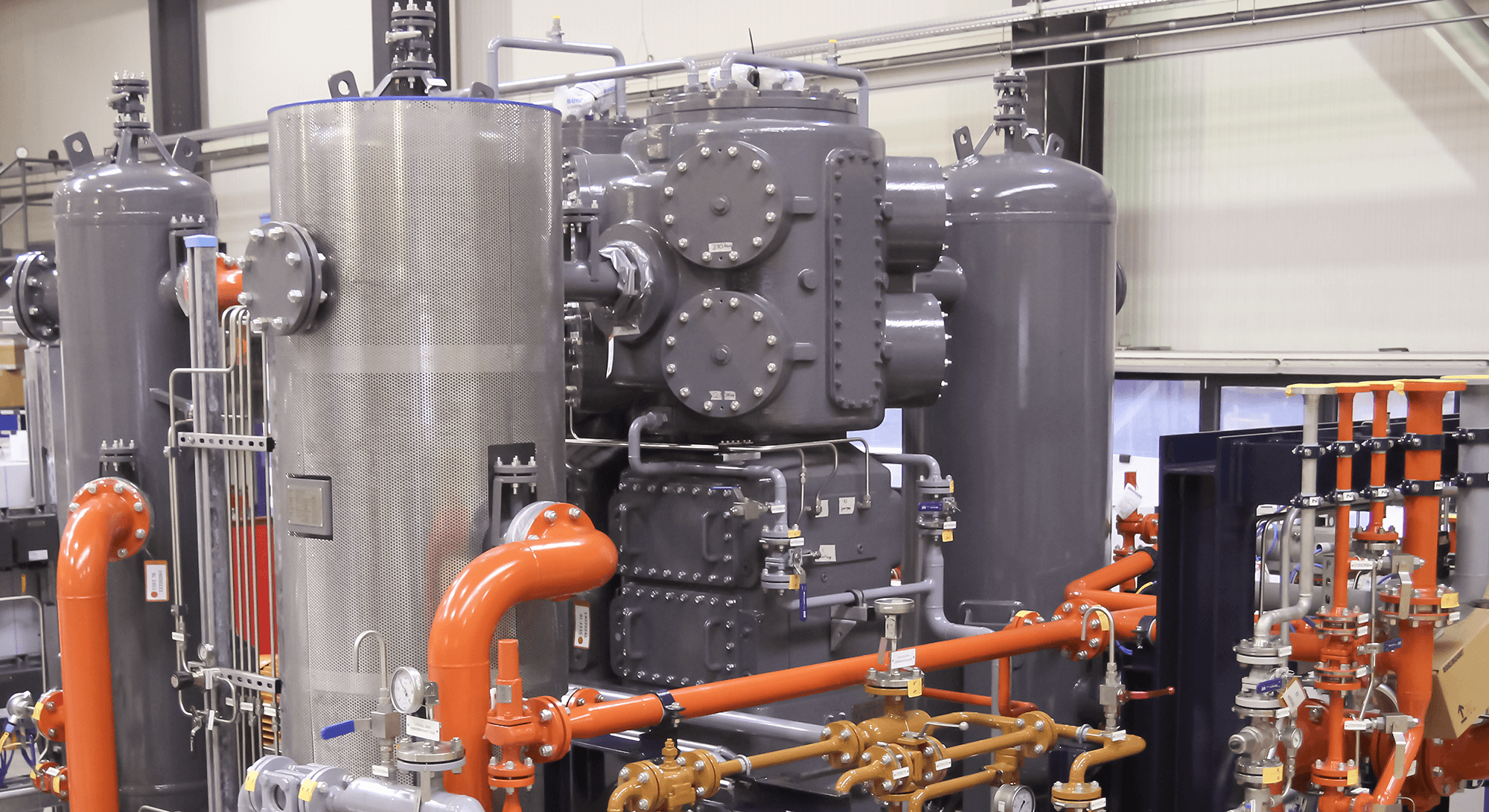 Pictured is a dark gray, standing reciprocating compressor of the PV series with pulsation vessels in BZM's assembly hall.